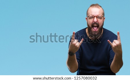 Young caucasian hipster man wearing sunglasses over isolated background shouting with crazy expression doing rock symbol with hands up. Music star. Heavy concept.