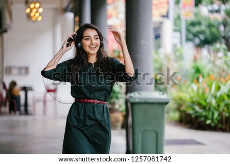 Portrait of a young, attractive and beautiful Indian Asian millennial girl dancing as she listens to music on her headphones. She is streaming music on her smartphone and is enjoying it as she dances.