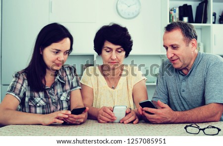 Cheerful senior couple and young woman using mobile phones while sitting together at home. Focus on young woman