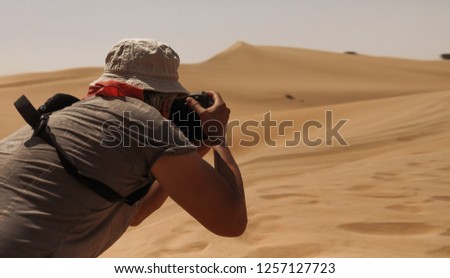 Professional traveller and photographer taking amazing pictures of the nature landscapes in desert. Yellow hot sand and dunes, nobody is around. Hat on the head protects from sun. African climate