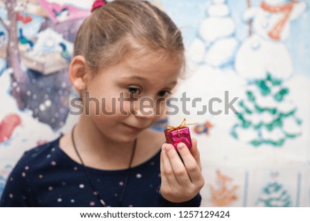 funny five-year-old girl with a pigtail surprised looking at a tiny gift against the backdrop of the winter picture