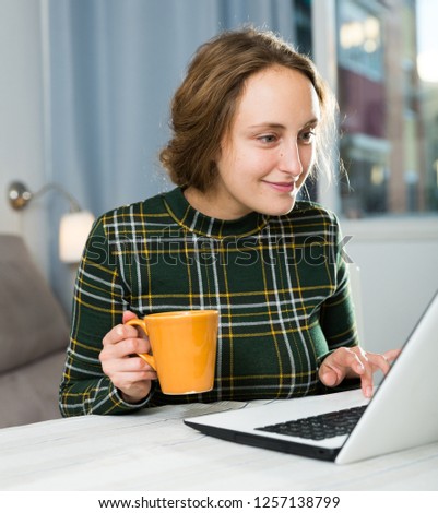 Attractive young woman using laptop and drinking tea at home