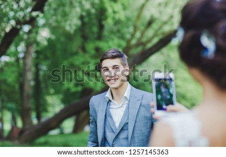 the bride takes pictures of the groom on his phone on the wedding day