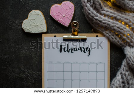 Flat lay calendar with clipboard and pencil on dark background. February 2019. top view. hearts cookies,