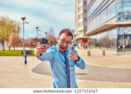 Funny businessman with thumbs up while using smartphone outdoors.