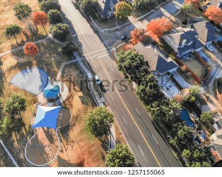 Aerial view park playground near residential area and local street in suburban Dallas, Texas, USA. Colorful fall leaves surround urban park with pathway and basketball court in early autumn morning