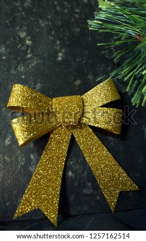 Yellow shiny bow and Christmas tree branch lies on gray background.