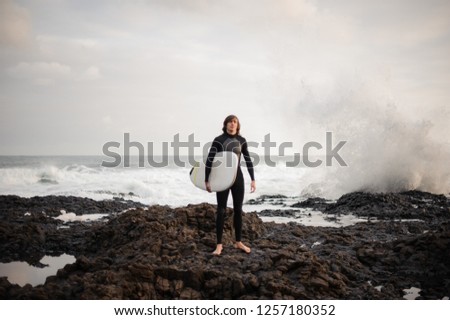 Man standing with a white surf in his hands on the pebble beach in the background of the sea.