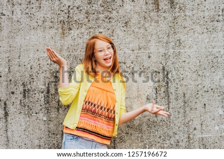 Outdoor portrait of pretty little girl with red hair, wearing orange t-shirt and yellow jacket