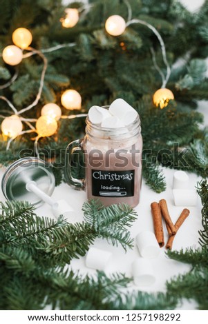Glass jar with cocoa and marshmallow, spruce branches with lights on background. Christmas loading