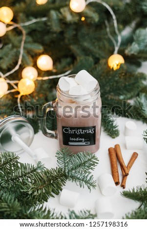 Glass jar with cocoa and marshmallow, spruce branches with lights on background. Christmas loading