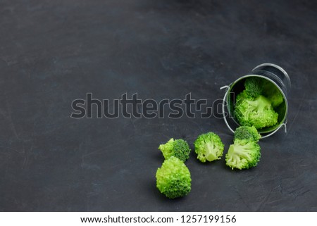 a placer of green broccoli cabbages from a small bucket. Template of healthy food on a dark background. Copy space vertical view. Vegetarian food. syroedenie.