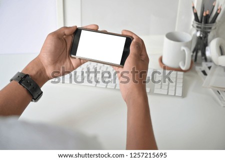 Mockup smartphone on man hands empty display with office desk background.