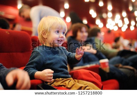 Cute toddler boy watching cartoon movie in the cinema. Leisure/entertainment for family with kids.
