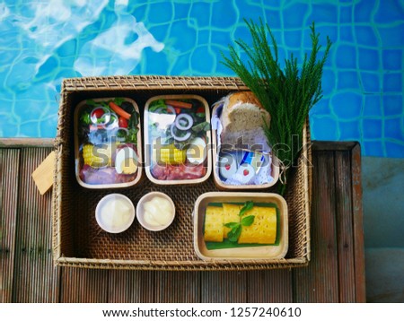 Breakfast is served in a basket on a wooden floor beside the pool, with fruit bread, jam, ham, bacon and boiled eggs