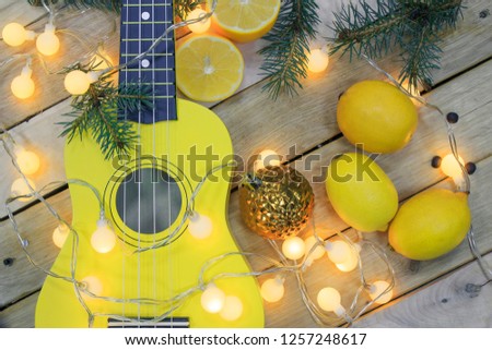 Photo of yellow Guitar, Fresh Orange Lemons, Fir-tree branches, Christmas tree toy and small light bulbs on Wooden Background. 