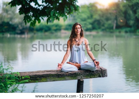 Woman doing yoga by the lake. Sitting in lotus position on a wooden quay. Royalty-Free Stock Photo #1257250207