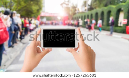 woman use mobile phone and blurred image of the crowd people beside the road of marathon racing at start point