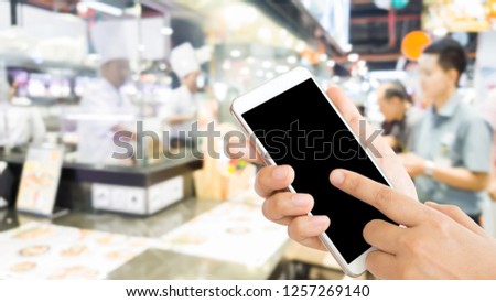 woman use mobile phone and blurred image of the restaurant with the customer bar and the chef show cooking