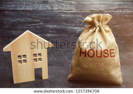 A bag with money and the word House and a wooden home. The concept of real estate purchase. Buy a house, apartment. Property. Affordable housing. Accumulation and saving money. Home rent