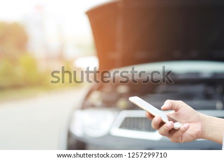 A man using mobile phone call emergency car service application because car was broken.
Using a mobile phone call a car mechanic.
A broken car on the road a roadside  is waiting for help.

