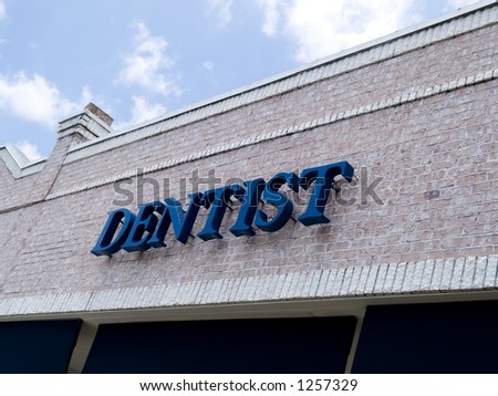 A sign for a dentist's office on the brick facade of a small building.