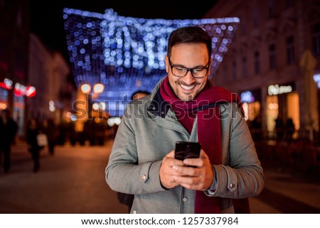 Handsome man texting at decorated city street at night. Front view.