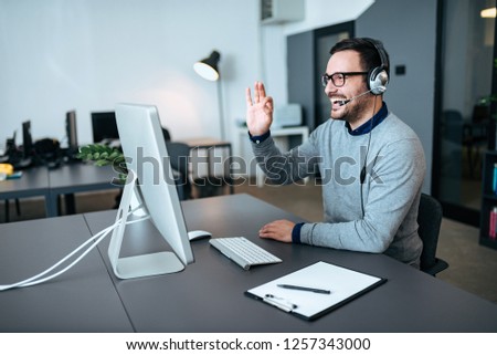 Handsome technical support agent talking to a client and giving him okay sign. Video call.