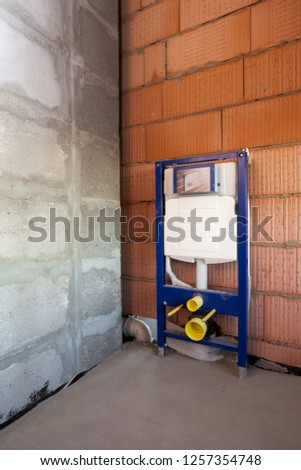 Vertical side view photo of concealed toilet carrier frame with flush tank mount on the red brick wall inside new comfort house