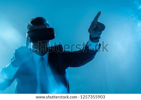 businessman in suit and virtual reality headset touching something isolated on blue, artificial intelligence concept