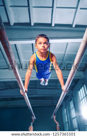The little boy is engaged in sports gymnastics on a parallel bars at gym. The performance, sport, acrobat, acrobatic, exercise, training concept