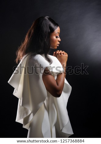 Portrait of a beautiful young African woman in white dress over black background. Studio picture