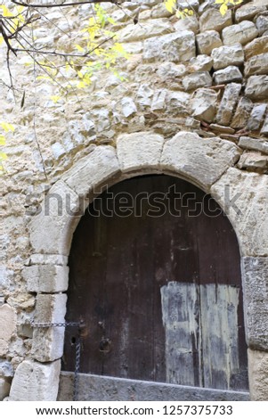 Close up front view of a stone window closed with weathered wooden planks. Yellow foliage at the foreground. Opening into an ancient wall with rounding shape. Isolated vintage element of architecture.