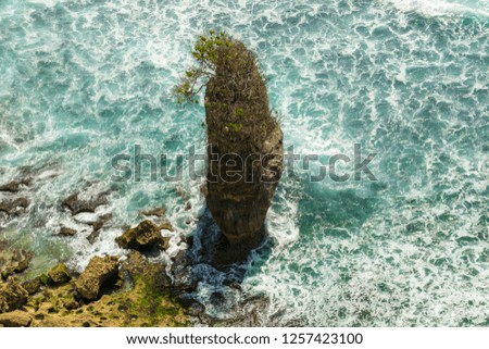 The Cliff and the sea, Uluwatu Beach, beautiful Bali, a rock by the sea with sea around it, waves reflecting the sunlight