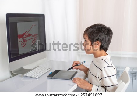  Schoolboy enthusiastically draw on a computer using a tablet in the room 