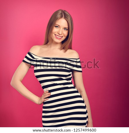 Beautiful toothy smiling blond long stright hairstyle woman in striped dress posing on pink background.