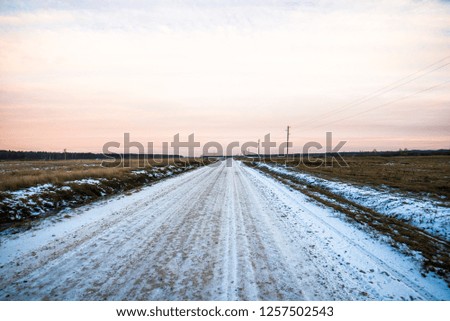 A dirt snow-covered country road through the fields at sunset. Forest in the background. Latvia