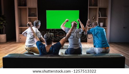 A group of students is watching a TV and celebrating some joyful sports moment, sitting on the couch in the living room. The living room is made in 3D. TV is green screen for further editing.