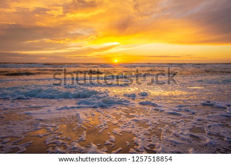 Colourful horizontal seascape landscape beach view with yellow sun in the middle, amazing sunset, foam heads left by the water on the beach, serene ocean view with an empty beach in the Netherlands 