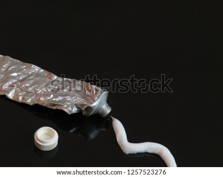 White cream being squeezed out of a metal ointment tube in a squiggly line onto a reflective back surface with room for text (copy).