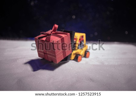 Miniature Gift Box by Forklift Machine on snow ,Determined Image for Christmas Holiday and Happy New Year Gift Celebration concept. Selective focus