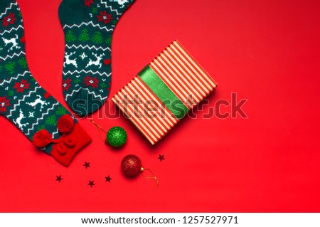 Woolen socks with a Christmas New Year ornament, gift box, balls, glitter confetti on red background top view flat lay. Holiday concept, presents Xmas. Congratulations background with space for text.