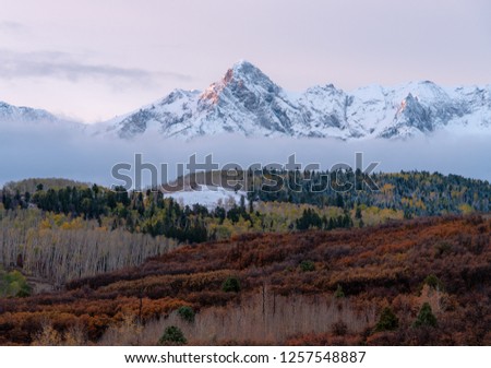 Snow capped peaks rise to meet pastel sunset colored skies in the Colorado Rockies on a crisp fall day