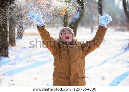 a boy in a warm jacket, hat and gloves throws snowballs over himself in a winter park
