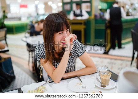 A Chinese Asian lady enjoys high tea with a good friend at a restaurant. She is beautiful, elegant and is smiling as she talks animatedly with her friend over cakes and tea on a weekend.