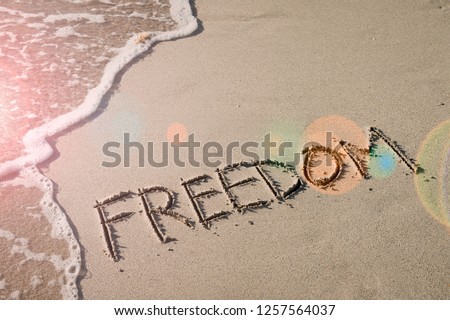 Freedom message handwritten in smooth sand with inspirational lens flare next to oncoming wave