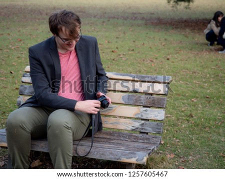 A man sat on a park bench taking pictures with his digital camera
