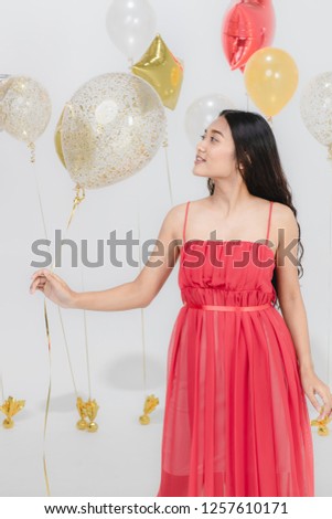 Beautiful young asian woman in red dress, happy smiling at fun party while holding colorful  balloons. Studio portrait shot on white background.