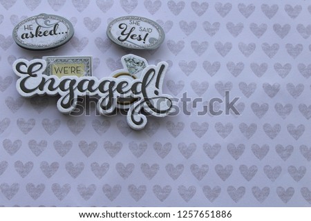 he asked she said yes we're engaged written in cursive in 3d on a background with silver hearts with writing space