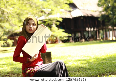 Half body portrait shot of beautiful Asian lady wearing green hijab with Malay's traditional attire "Kurung" holding sign board for text.